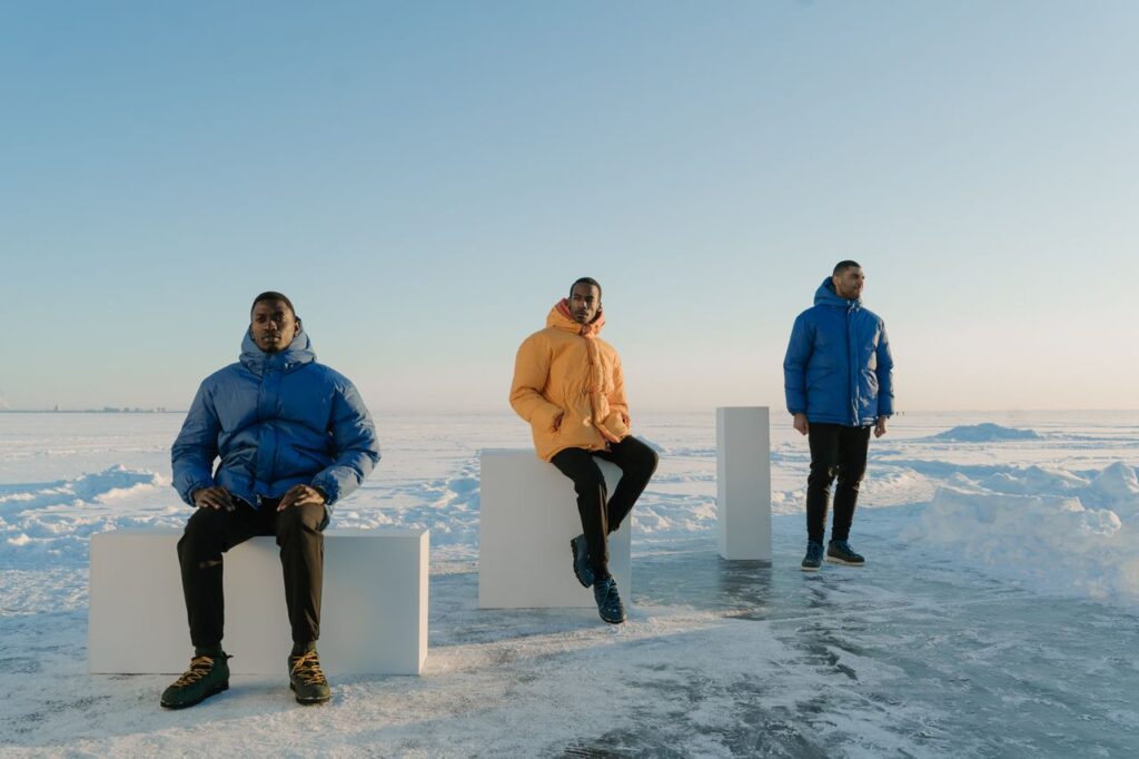 Three men in colorful puffer jackets pose on a snowy landscape with clear blue sky.